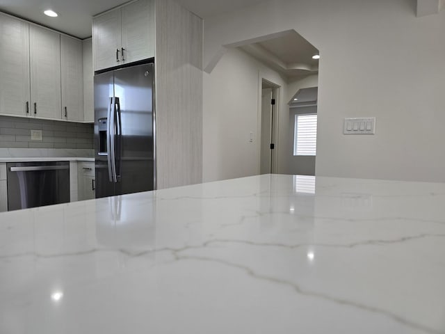 kitchen with backsplash, light stone countertops, white cabinets, and appliances with stainless steel finishes