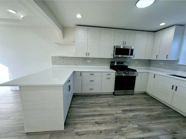 kitchen featuring white cabinetry, backsplash, stainless steel appliances, and kitchen peninsula