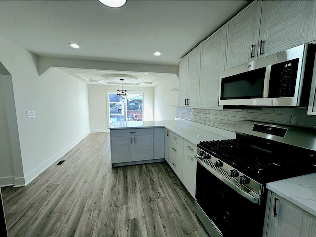 kitchen featuring tasteful backsplash, decorative light fixtures, appliances with stainless steel finishes, kitchen peninsula, and light stone countertops