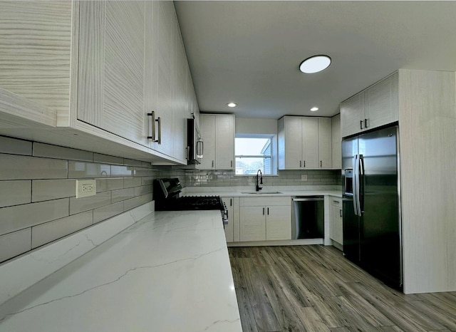 kitchen featuring dishwashing machine, refrigerator with ice dispenser, sink, black stove, and decorative backsplash