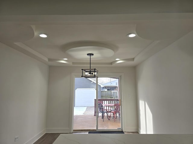 unfurnished dining area featuring hardwood / wood-style floors, a tray ceiling, and a notable chandelier