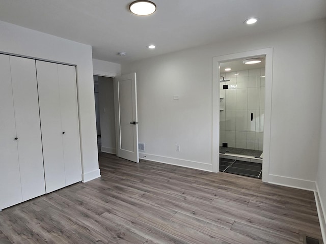 unfurnished bedroom with ensuite bathroom, hardwood / wood-style floors, and a closet