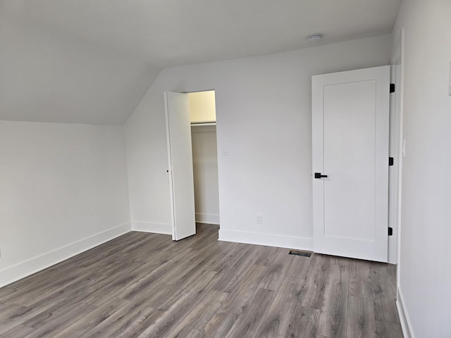 unfurnished bedroom featuring vaulted ceiling, a spacious closet, light hardwood / wood-style flooring, and a closet