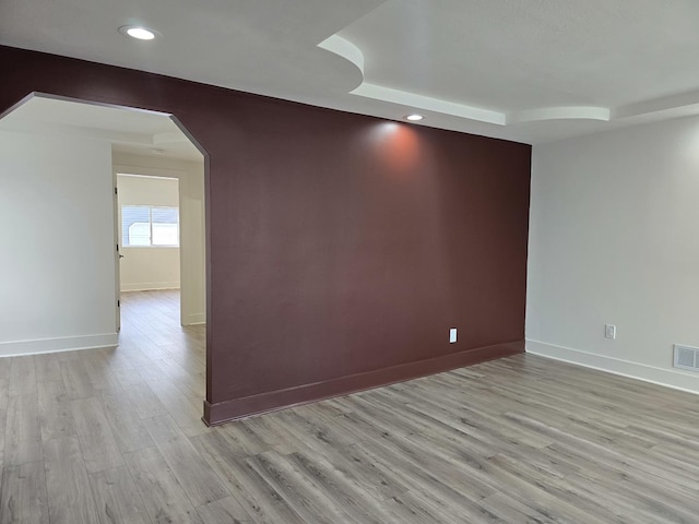 spare room featuring a raised ceiling and light hardwood / wood-style flooring