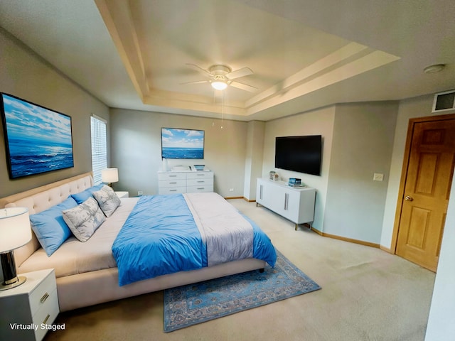 bedroom with light carpet, ceiling fan, and a raised ceiling