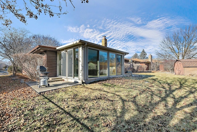 back of house with an outdoor structure, a lawn, a shed, a chimney, and a patio area