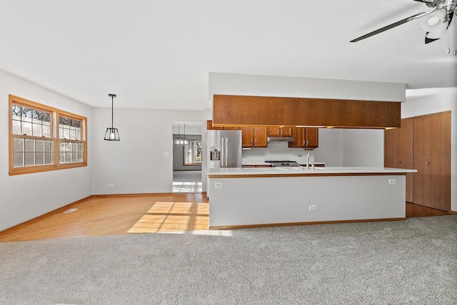 kitchen with brown cabinetry, appliances with stainless steel finishes, hanging light fixtures, light countertops, and under cabinet range hood