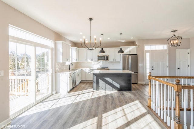 kitchen with appliances with stainless steel finishes, white cabinets, a kitchen island, sink, and decorative light fixtures