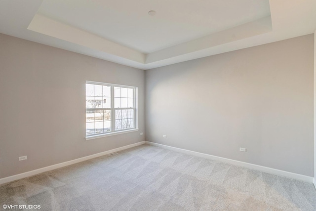 unfurnished room with light colored carpet and a tray ceiling