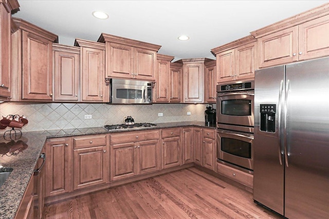 kitchen with dark stone countertops, stainless steel appliances, light wood-type flooring, and tasteful backsplash