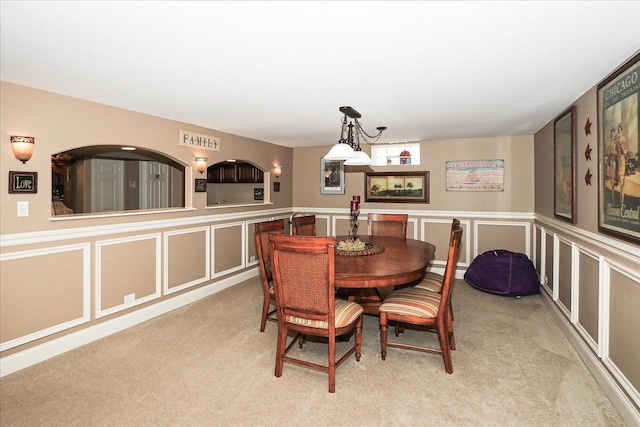 carpeted dining area featuring a wainscoted wall and a decorative wall