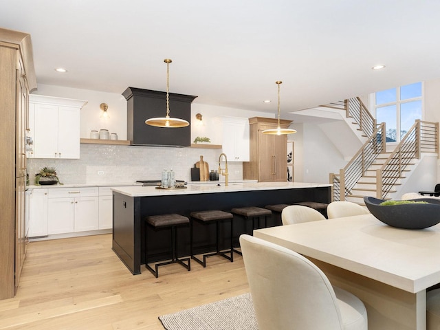 kitchen featuring hanging light fixtures, a breakfast bar, an island with sink, and white cabinetry