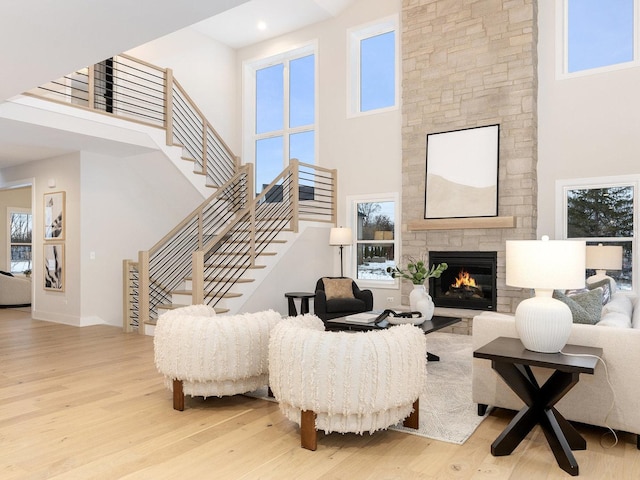 living room featuring light hardwood / wood-style floors, a towering ceiling, and a stone fireplace