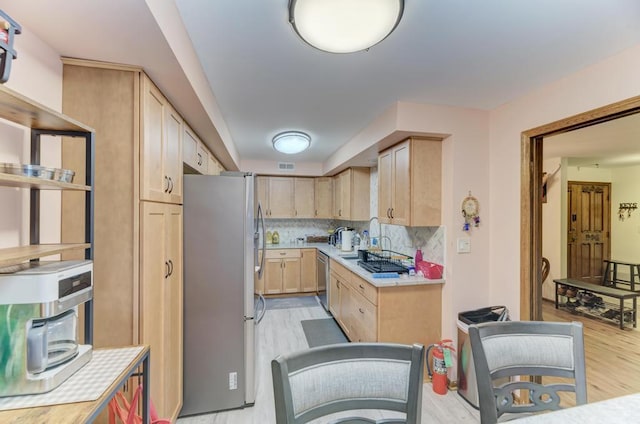 kitchen featuring light brown cabinetry, sink, light wood-type flooring, tasteful backsplash, and stainless steel appliances