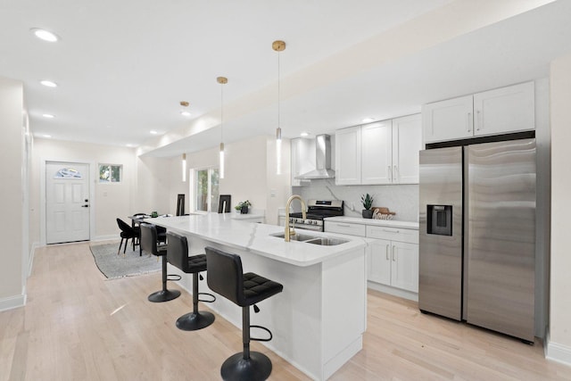 kitchen with backsplash, pendant lighting, appliances with stainless steel finishes, white cabinets, and wall chimney exhaust hood