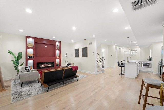 living room with light wood-type flooring, a large fireplace, and sink