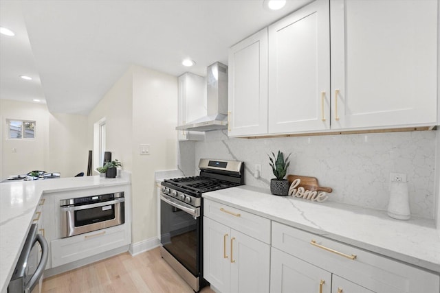 kitchen featuring light stone countertops, decorative backsplash, appliances with stainless steel finishes, and wall chimney exhaust hood