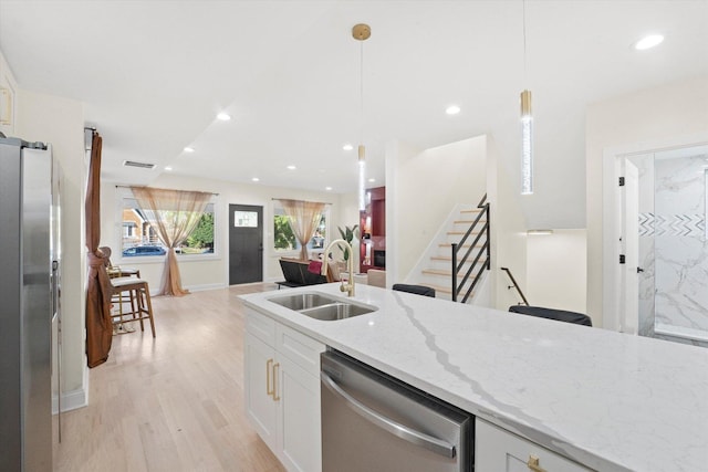 kitchen featuring pendant lighting, white cabinets, stainless steel appliances, sink, and light stone counters