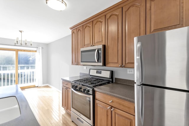 kitchen featuring pendant lighting, stainless steel appliances, an inviting chandelier, sink, and light wood-type flooring