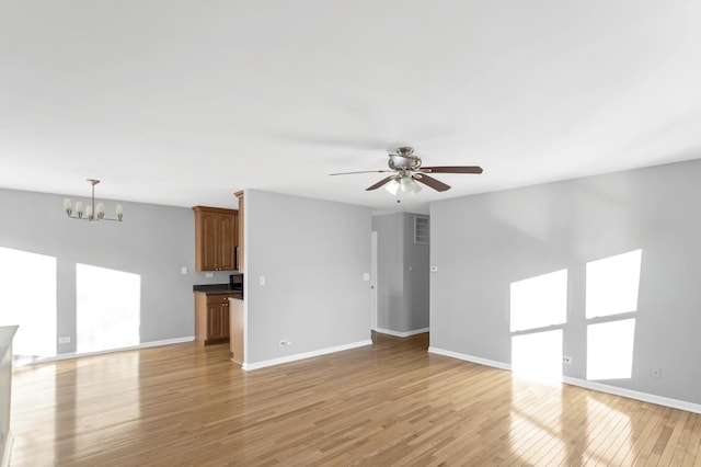 unfurnished living room featuring ceiling fan with notable chandelier and light wood-type flooring