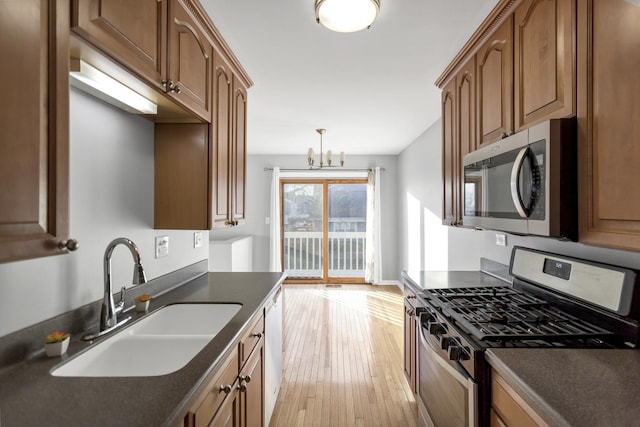 kitchen with light hardwood / wood-style floors, stainless steel appliances, a notable chandelier, hanging light fixtures, and sink