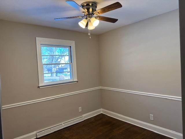 spare room featuring ceiling fan, a baseboard heating unit, and dark hardwood / wood-style floors