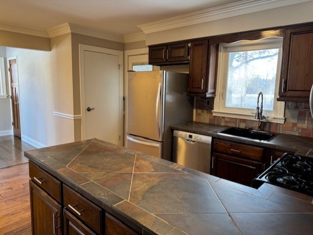 kitchen with dark brown cabinetry, appliances with stainless steel finishes, light hardwood / wood-style floors, sink, and crown molding