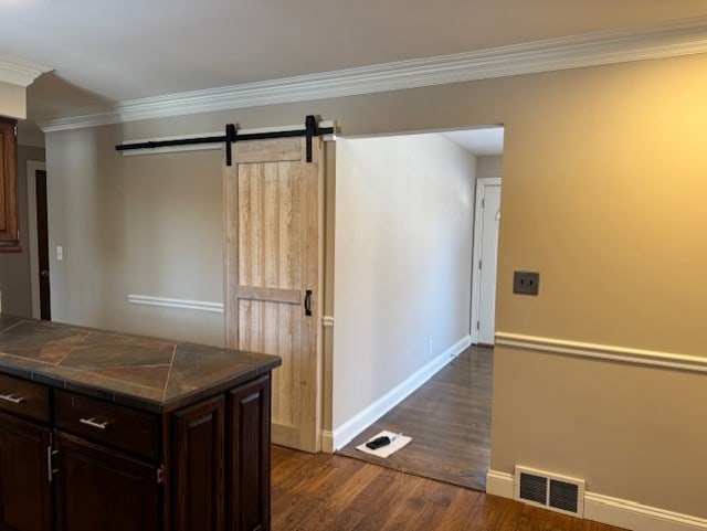 kitchen featuring dark wood-type flooring, dark brown cabinetry, crown molding, and a barn door