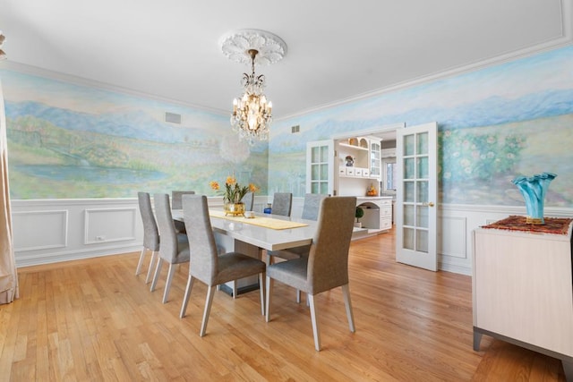 dining room featuring french doors, ornamental molding, light hardwood / wood-style flooring, and a notable chandelier