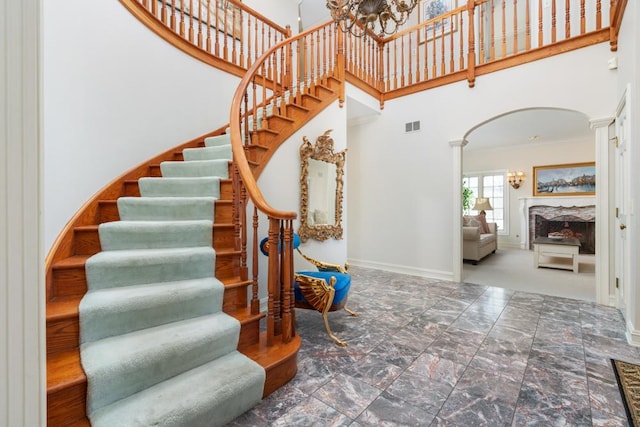 stairs featuring a towering ceiling, an inviting chandelier, and decorative columns