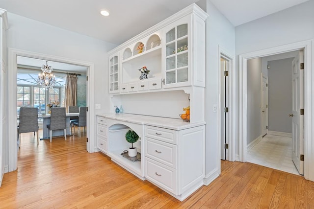 bar featuring light hardwood / wood-style floors, light stone countertops, white cabinets, and a chandelier