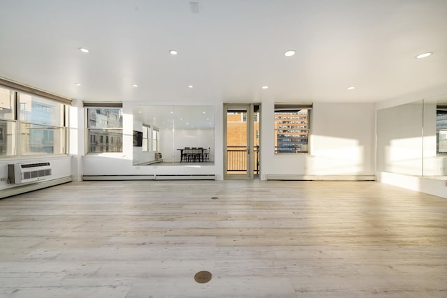 unfurnished living room with a wall unit AC, light hardwood / wood-style flooring, and a baseboard heating unit