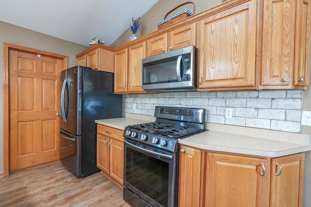 kitchen featuring light wood-type flooring, appliances with stainless steel finishes, lofted ceiling, and tasteful backsplash