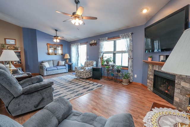 living room with lofted ceiling, wood-type flooring, a stone fireplace, and ceiling fan