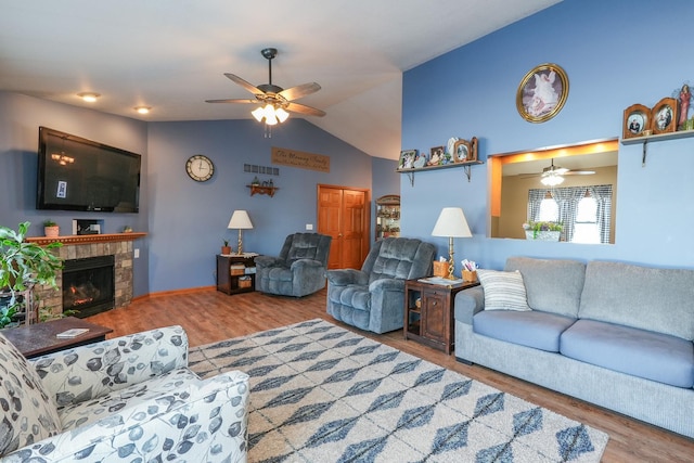 living room featuring ceiling fan, lofted ceiling, wood-type flooring, and a stone fireplace