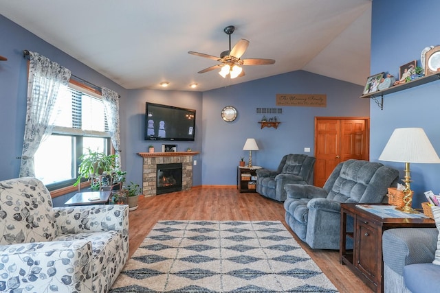 living room featuring ceiling fan, vaulted ceiling, a stone fireplace, and light wood-type flooring