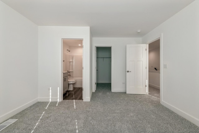 unfurnished bedroom with a walk in closet, a closet, ensuite bath, and carpet flooring