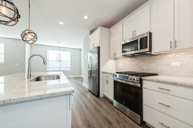 kitchen featuring white cabinets, appliances with stainless steel finishes, decorative light fixtures, an island with sink, and sink