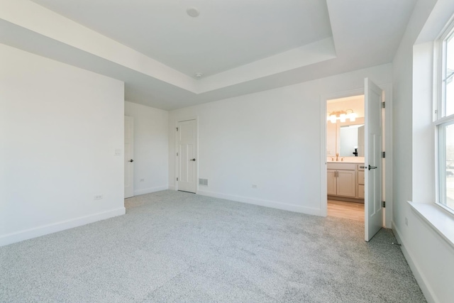 unfurnished bedroom featuring a raised ceiling, light carpet, sink, and connected bathroom