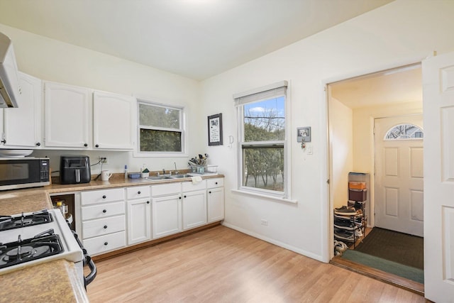 kitchen with sink, white cabinetry, white gas stove, and light hardwood / wood-style flooring