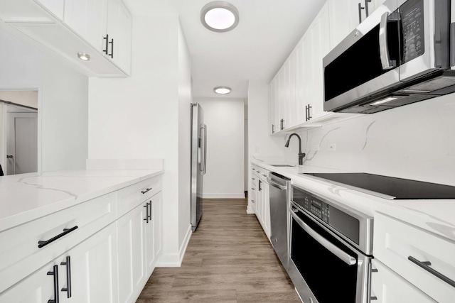 kitchen with light wood finished floors, appliances with stainless steel finishes, light stone countertops, white cabinetry, and a sink