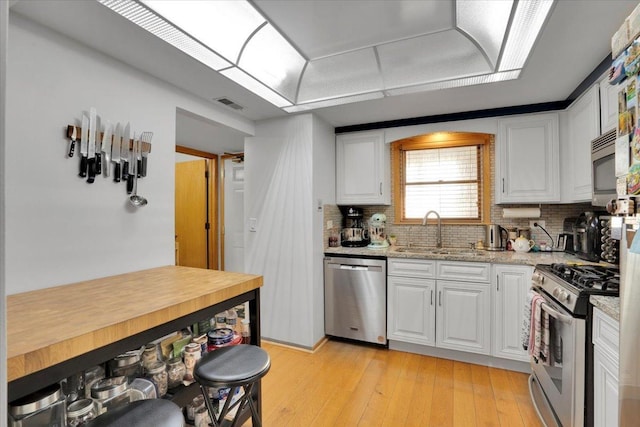 kitchen featuring light hardwood / wood-style floors, light stone countertops, appliances with stainless steel finishes, white cabinets, and sink