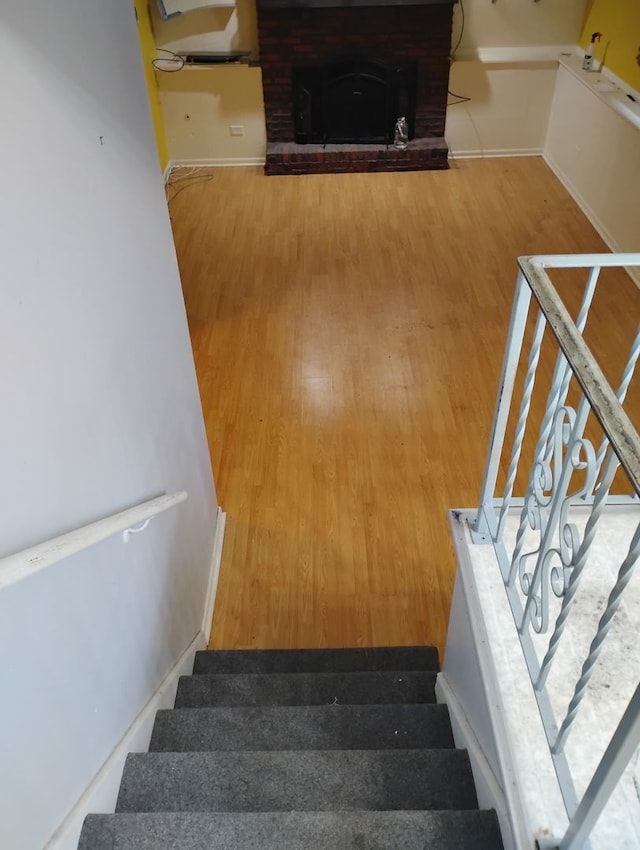 staircase with a brick fireplace and wood-type flooring