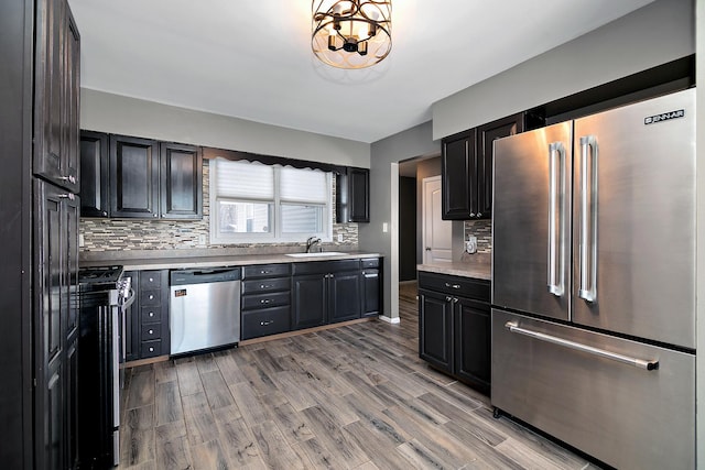 kitchen featuring appliances with stainless steel finishes, sink, light wood-type flooring, decorative backsplash, and an inviting chandelier