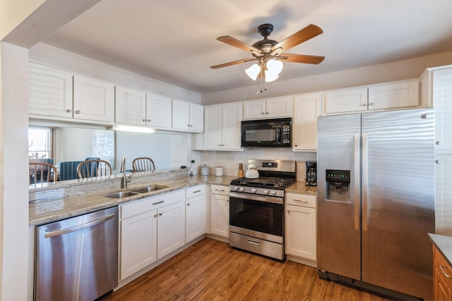 kitchen with light stone countertops, white cabinets, stainless steel appliances, sink, and light wood-type flooring