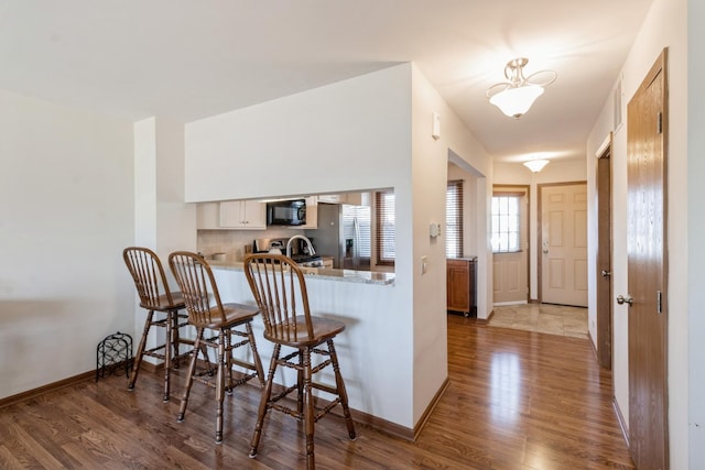 kitchen with white cabinets, wood-type flooring, stainless steel fridge with ice dispenser, kitchen peninsula, and a breakfast bar area