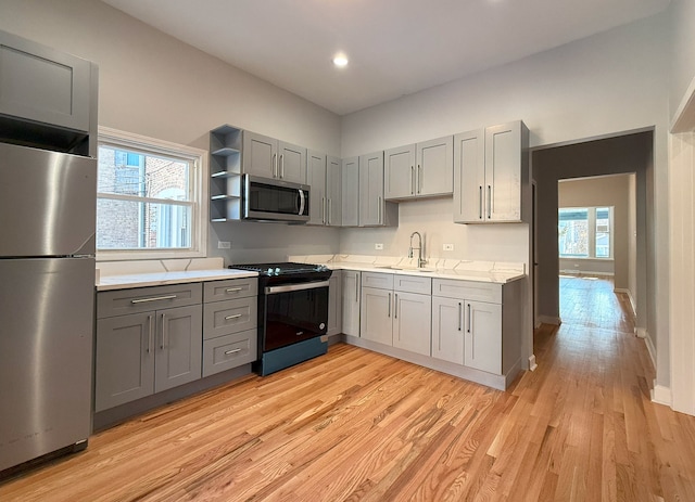 kitchen with stainless steel appliances, sink, gray cabinetry, and light hardwood / wood-style flooring