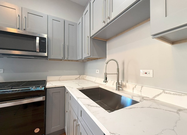 kitchen featuring sink, gray cabinets, light stone countertops, and gas stove