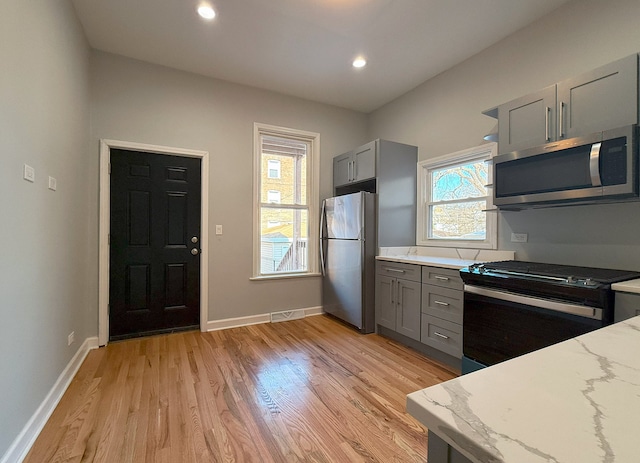 kitchen featuring appliances with stainless steel finishes, plenty of natural light, gray cabinetry, light hardwood / wood-style floors, and light stone countertops