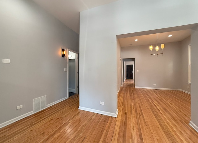 empty room featuring an inviting chandelier, a towering ceiling, and light wood-type flooring